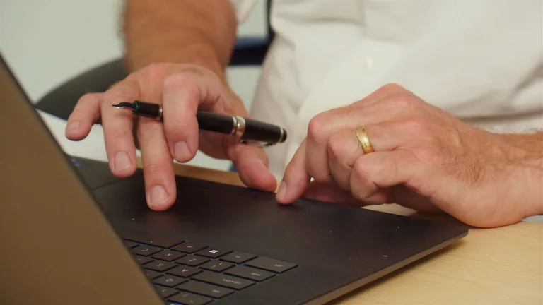 Close-up of hands at a laptop keyboard, a fountain pen between the fingers