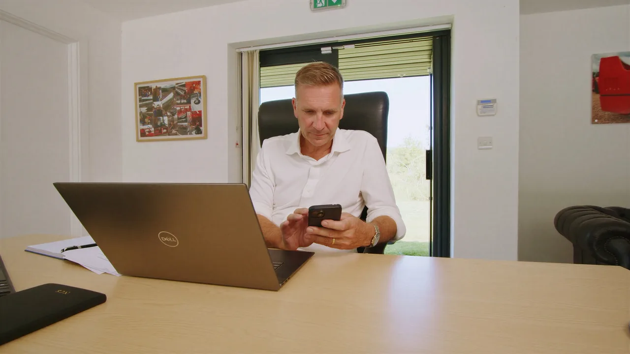 At a desk in the Stratworth Advisory office, laptop open, checking a phone