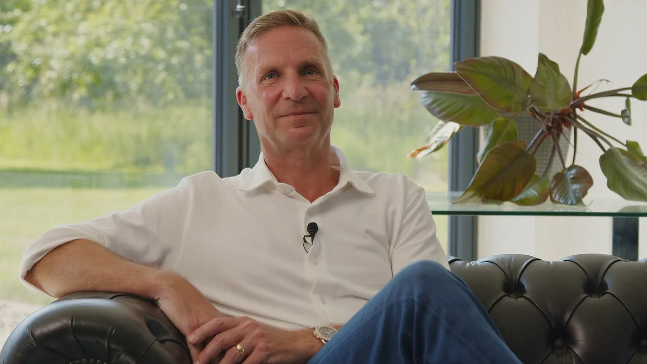 Seated in a leather armchair in the Stratworth Advisory office, smiling
