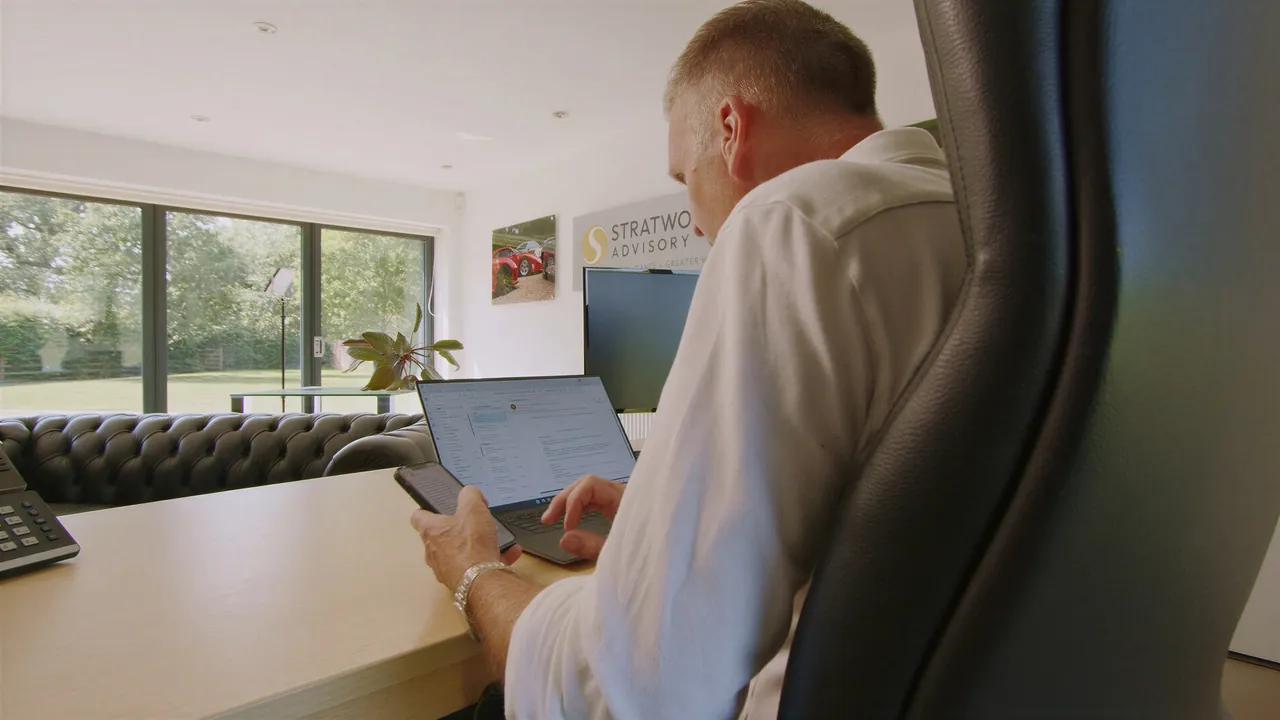Working at a laptop in the Stratworth Advisory office, with tall windows onto the garden