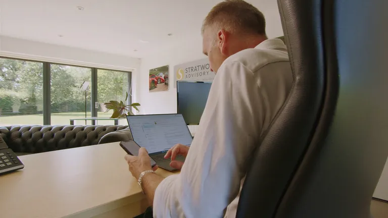 Working at a laptop in the Stratworth Advisory office, with tall windows onto the garden