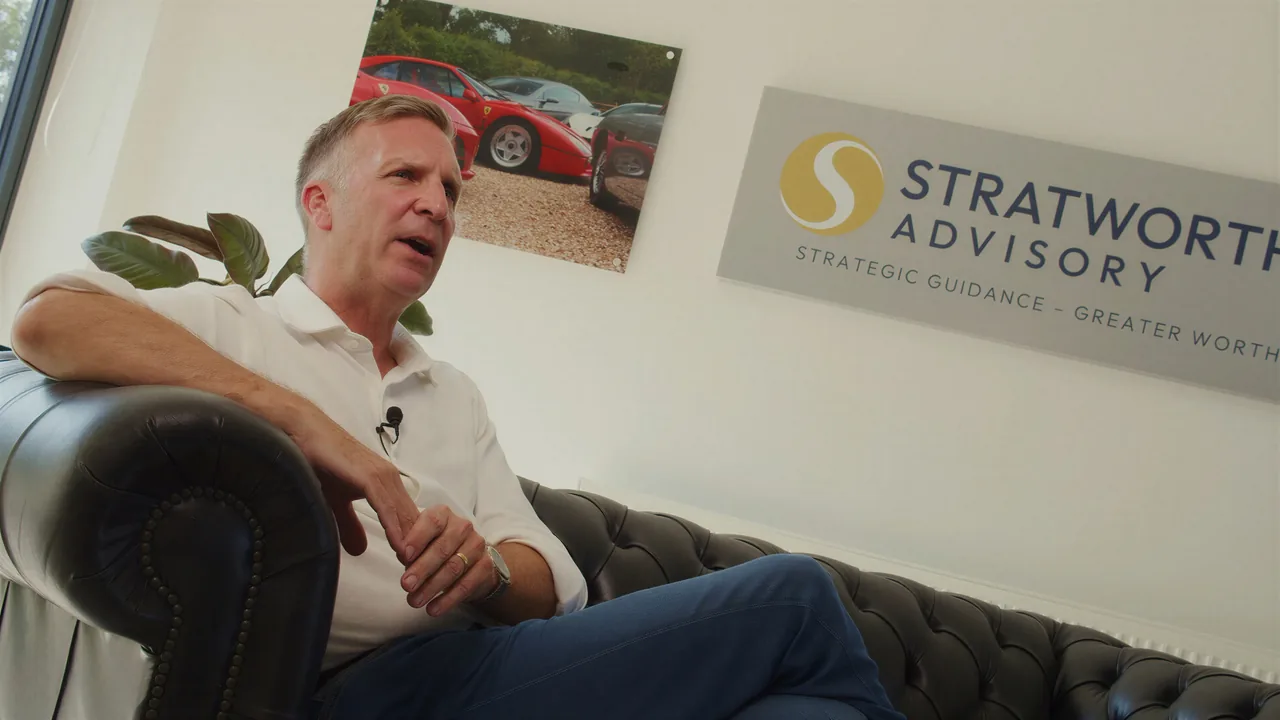 Seated on a leather sofa beneath the Stratworth Advisory sign, listening